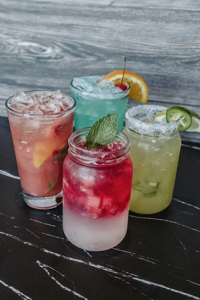 Four colorful, garnished drinks on a dark marble surface.