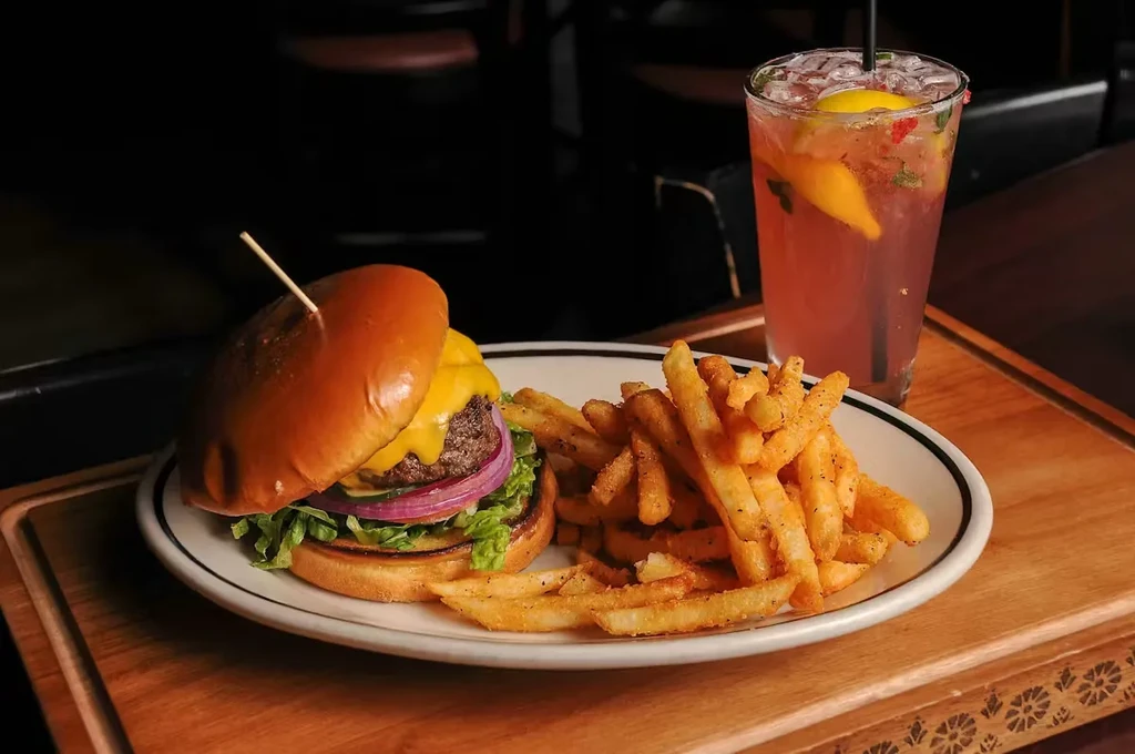 Cheeseburger, french fries, and pink drink on a wooden surface.