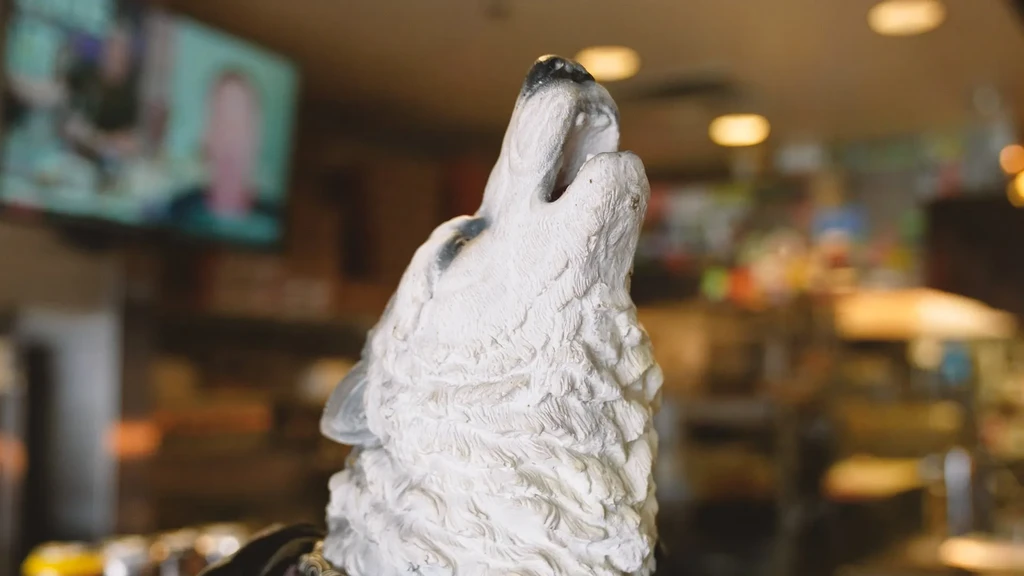 Textured white wolf head sculpture howling upwards, blurred interior.
