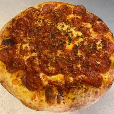 Overhead view of a well-cooked pepperoni pizza with melted cheese and herbs.