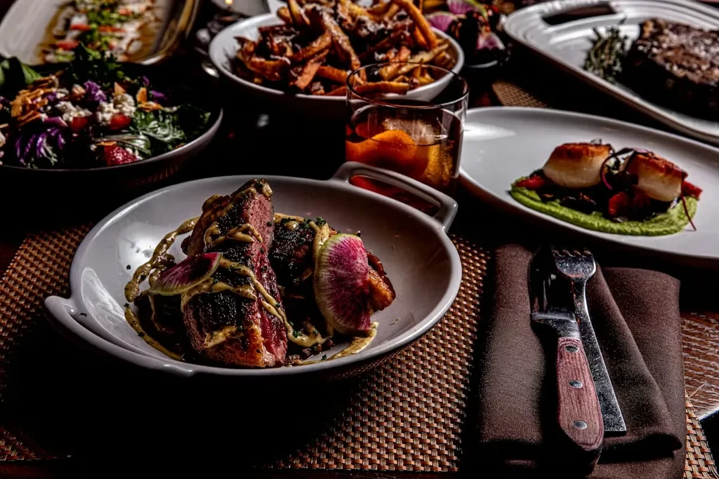 Gourmet restaurant meal: seared duck, scallops, fries, salad, and cocktail.
