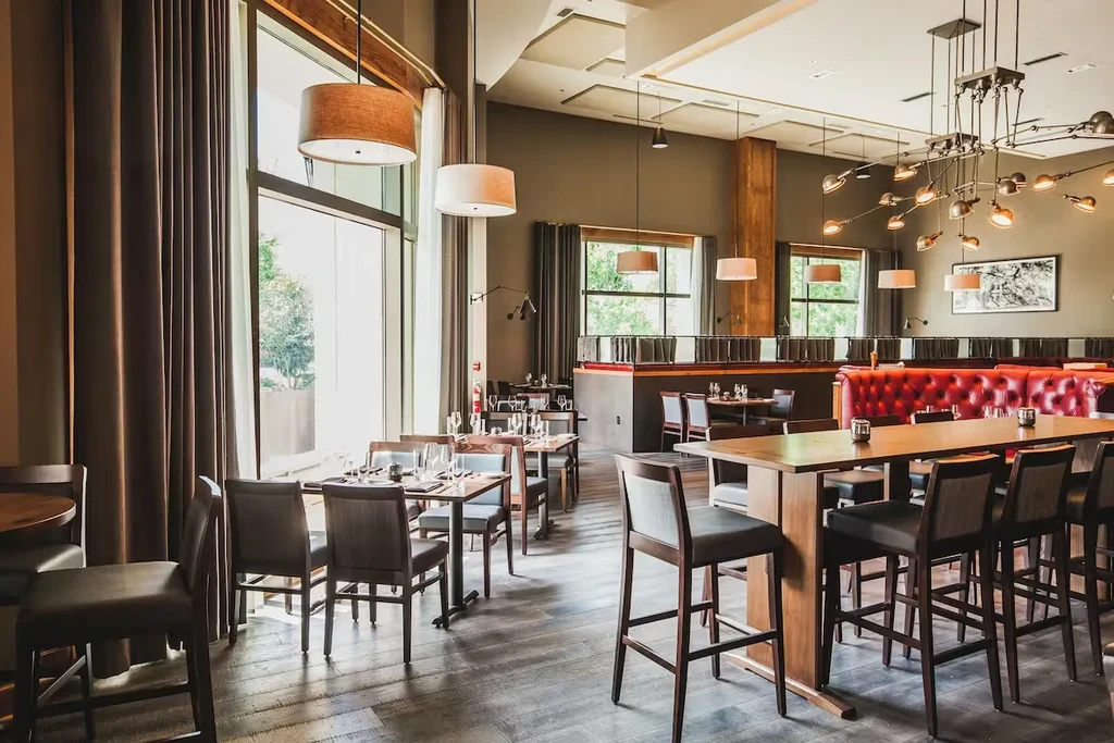 Modern restaurant interior with high-top, red booths, large windows, no people.