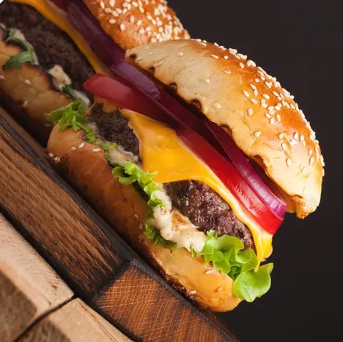 Two hamburgers with cheese, lettuce, onion, and sauce on rustic wood.
