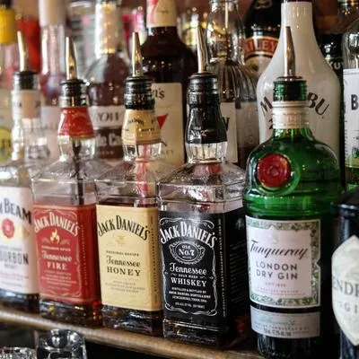 Well-stocked bar shelf with various liquor bottles and pour spouts.
