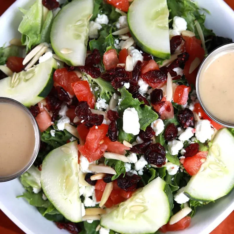 Green salad with cucumber, tomato, feta, cranberries, almonds, and dressing.