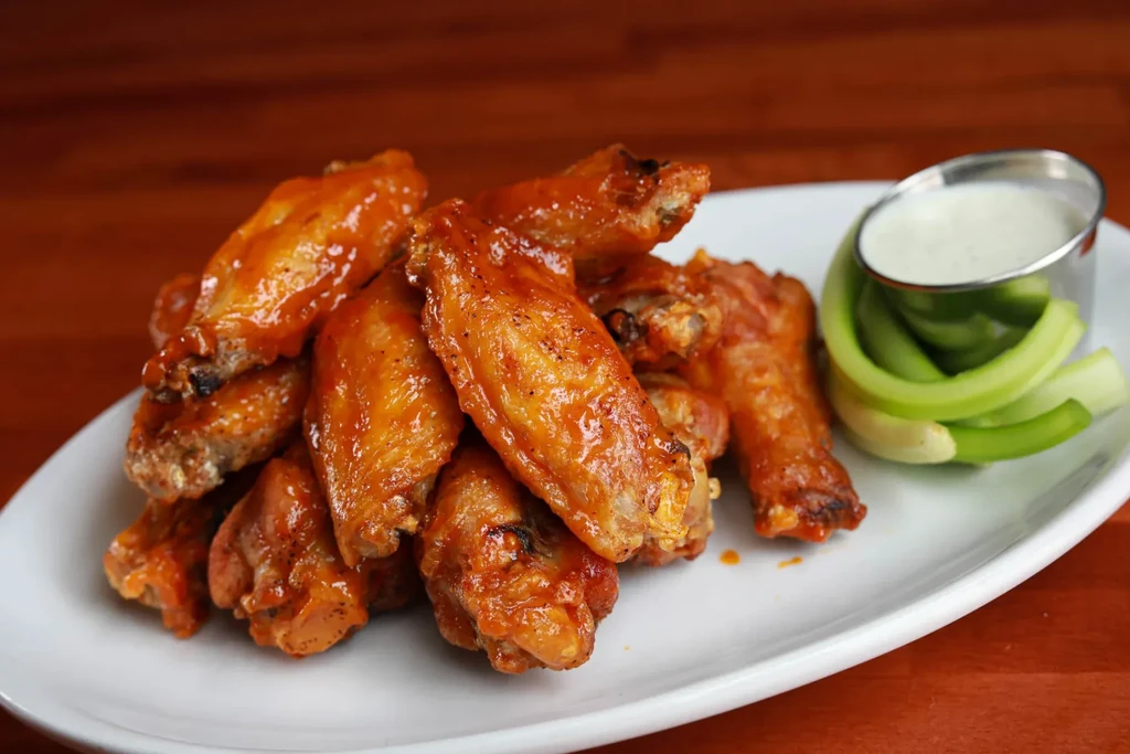 A plate of piled buffalo chicken wings, creamy dip, and celery.