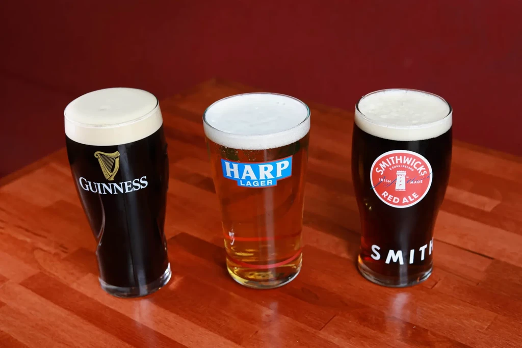 Three glasses of Guinness, Harp, Smithwick's beers on a wooden bar.