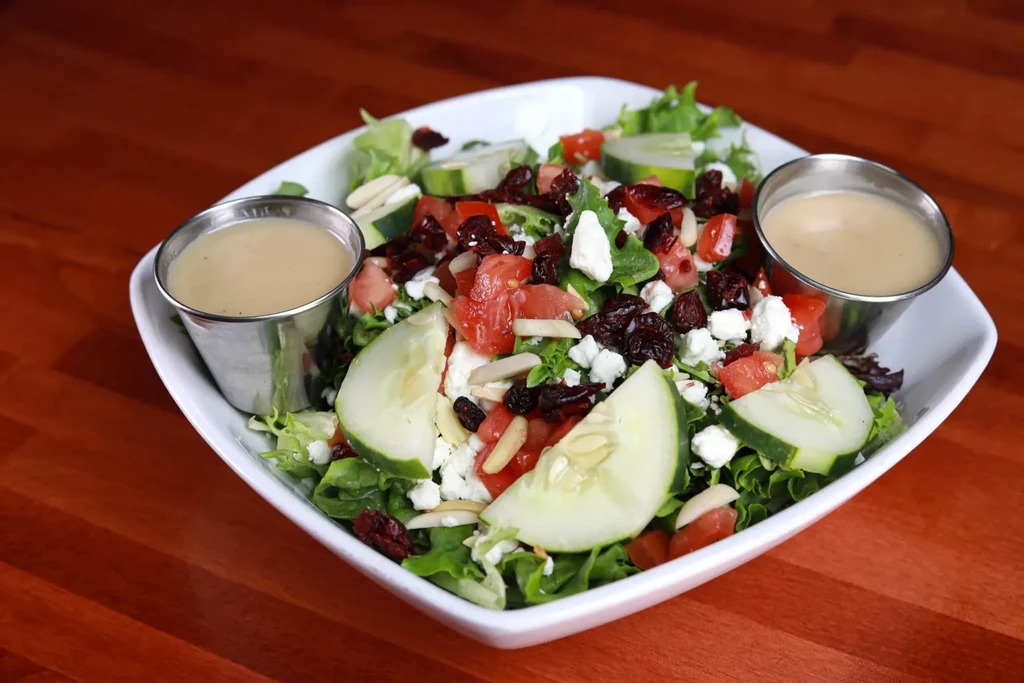 Mixed green salad with cucumbers, tomatoes, feta, almonds, cranberries, and two dressings.
