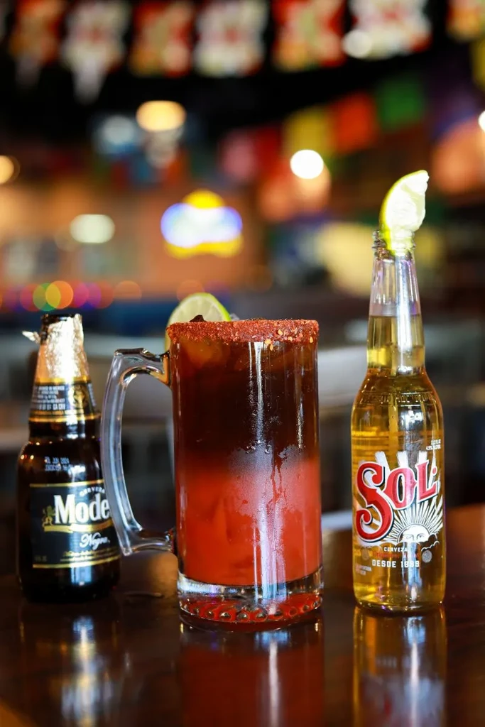Modelo Negra, rimmed Michelada, and Sol beer on a bar.