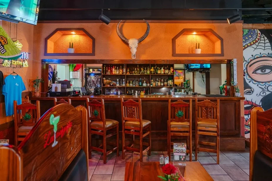 Vibrant Mexican bar interior with bull skull, agave stools, liquor.