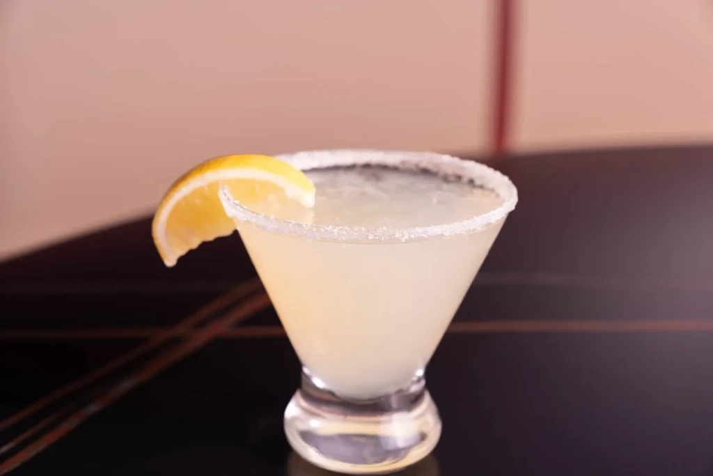 Citrus cocktail in martini glass with frosted rim and lemon garnish.