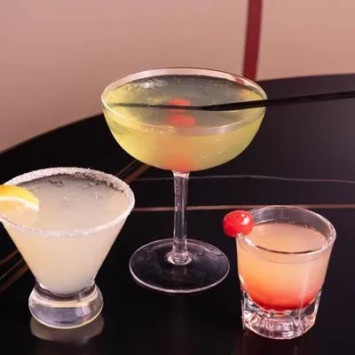 Three distinct, garnished cocktails on a dark reflective surface.