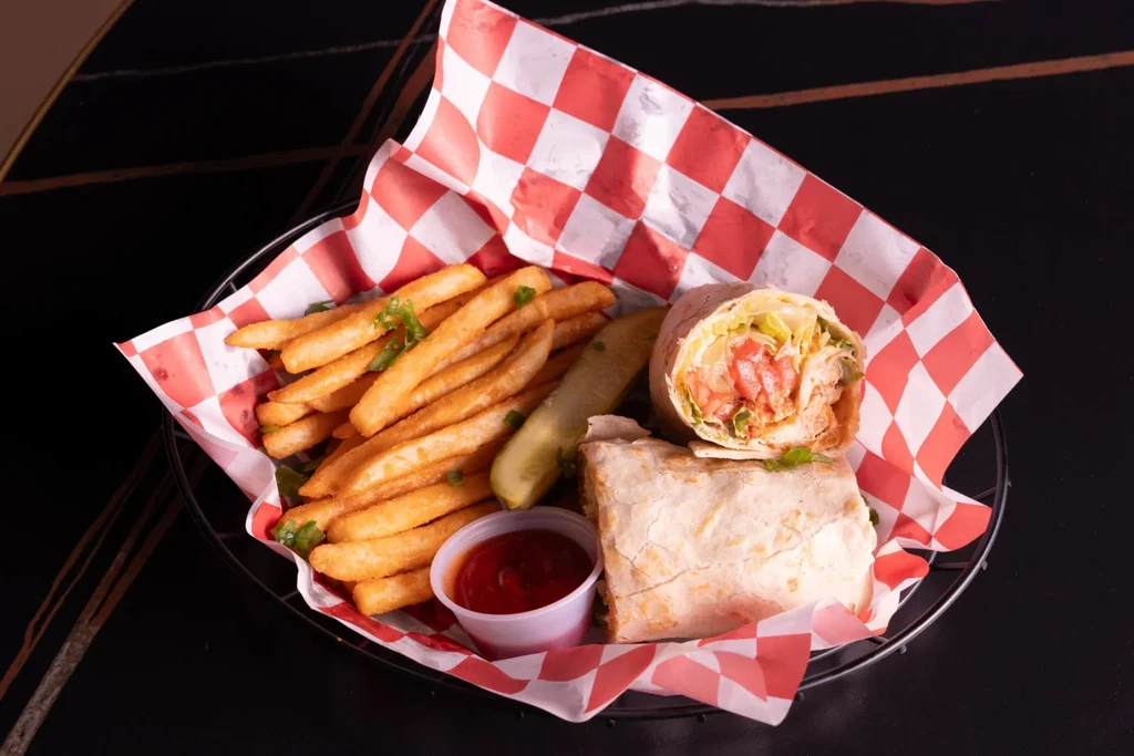 Fries, dill pickle, ketchup, and halved chicken wrap in a wire basket.