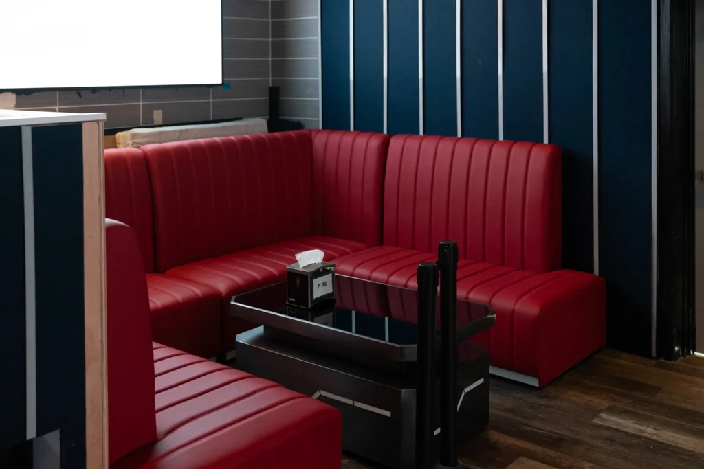 Modern private booth with red banquettes, glass table, and striped wall.