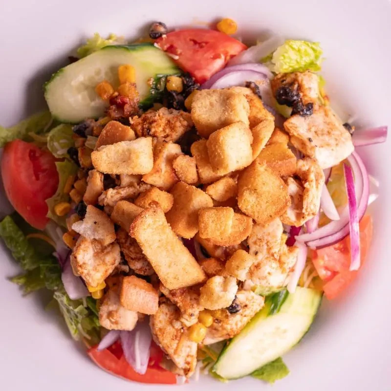 Fresh salad with grilled chicken, vegetables, and croutons in a white bowl.
