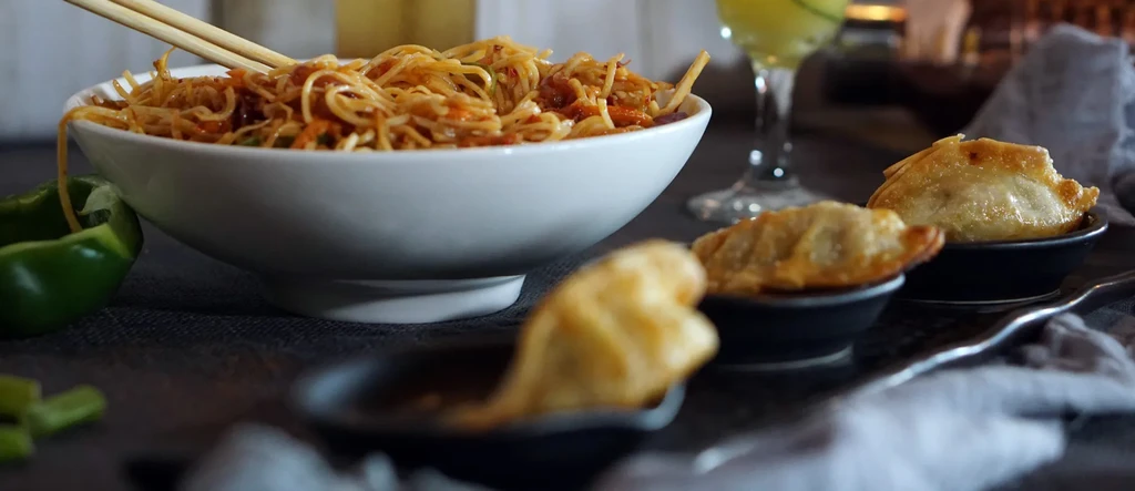 Close-up of Asian noodles with chopsticks, fried dumplings, and bell pepper.