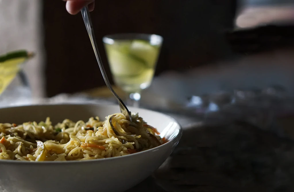 A fork lifts stir-fried noodles and vegetables from a bowl.