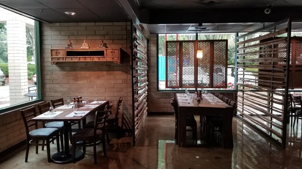 Empty restaurant dining room with communal table, brick walls, Buddha figurines.