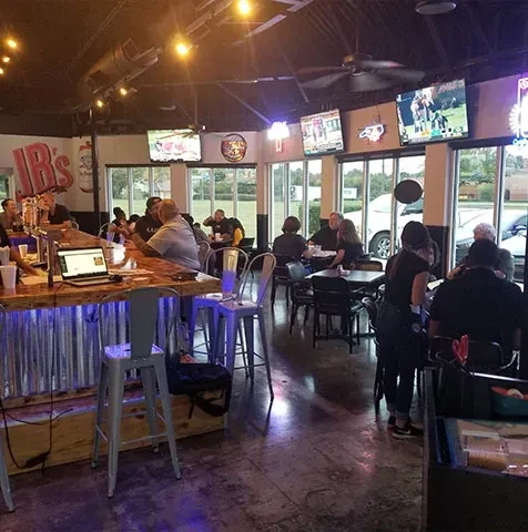 Busy, dim sports bar interior with purple-lit bar, TVs, and patrons.
