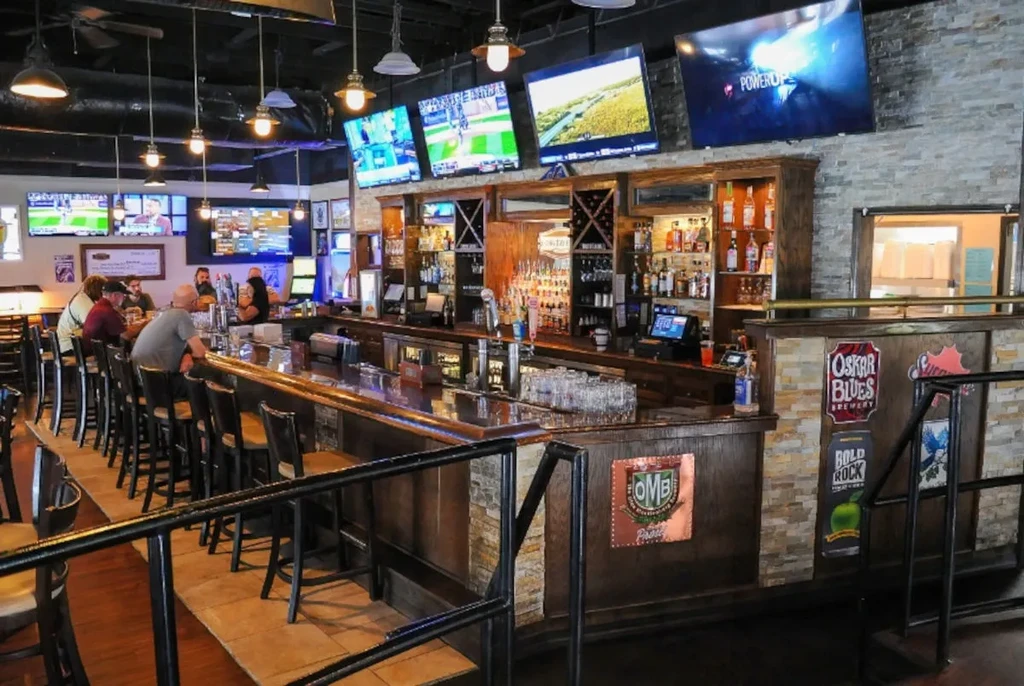 Lively sports bar interior with a wooden bar, TVs, and patrons.