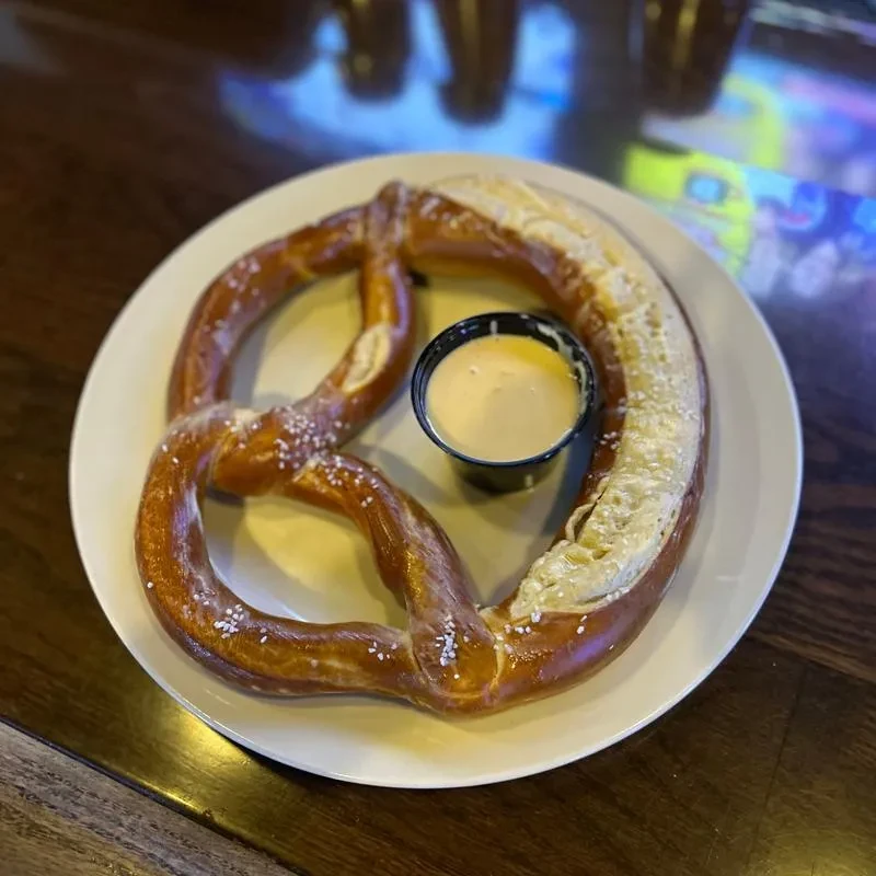 Large, golden-brown salted pretzel with a yellow cheese dip.