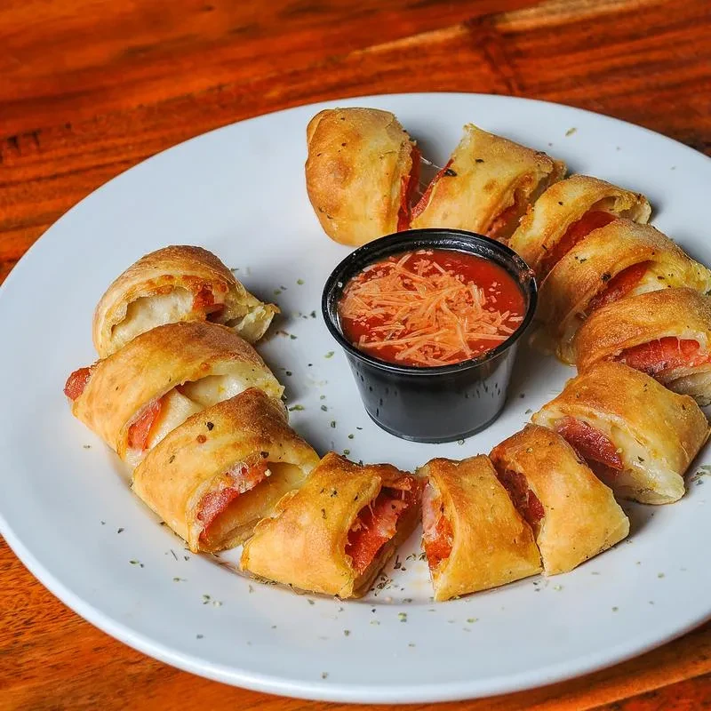 Gooey pepperoni pizza rolls surrounding marinara dip on a white plate.