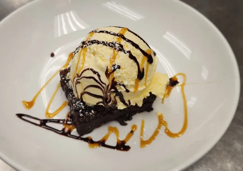 Dark brownie, vanilla ice cream, chocolate, caramel sauce, powdered sugar on plate.