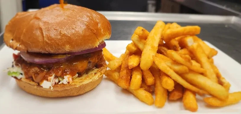 Hamburger with melted cheese, coleslaw, and seasoned fries on a plate.