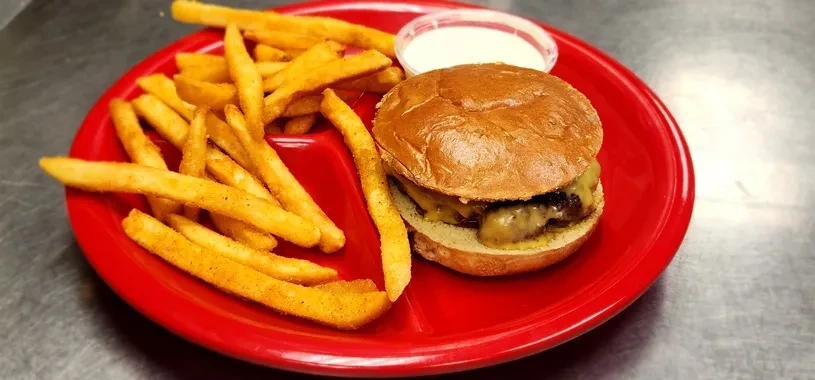 Cheeseburger and seasoned fries with dipping sauce on a red plate.