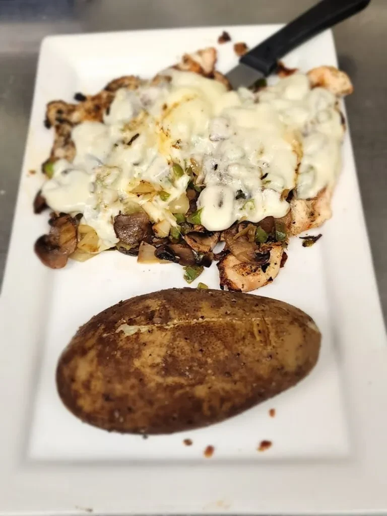 Plate of cheesy grilled chicken, sautéed vegetables, and a baked potato.
