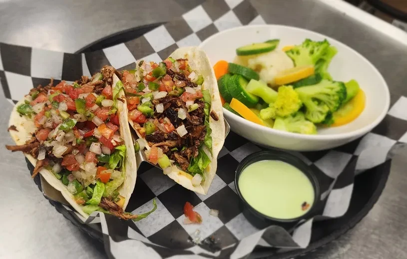 Two shredded meat soft tacos, pico de gallo, vegetables, and avocado crema.