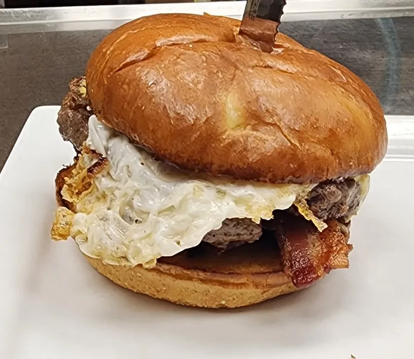 Burger with thick beef patty, fried egg, bacon, brioche bun, and knife.