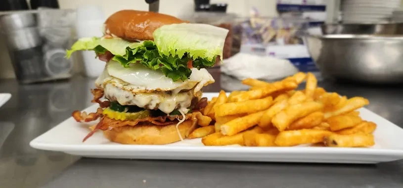 Towering gourmet burger with egg, bacon, cheese, and crinkle-cut fries.
