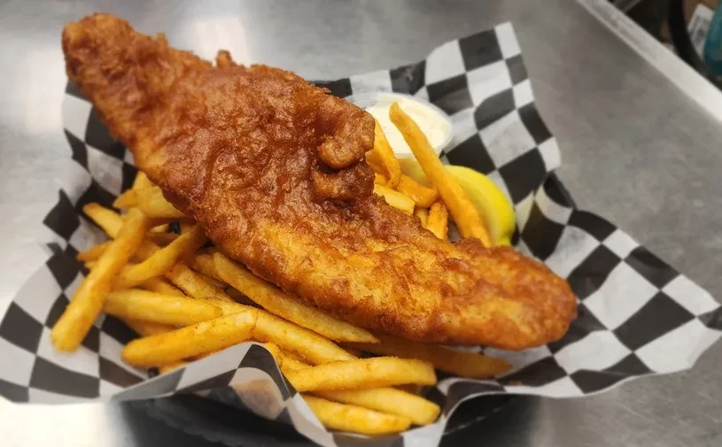 Crispy fish and golden fries in a basket with sauce and lemon.
