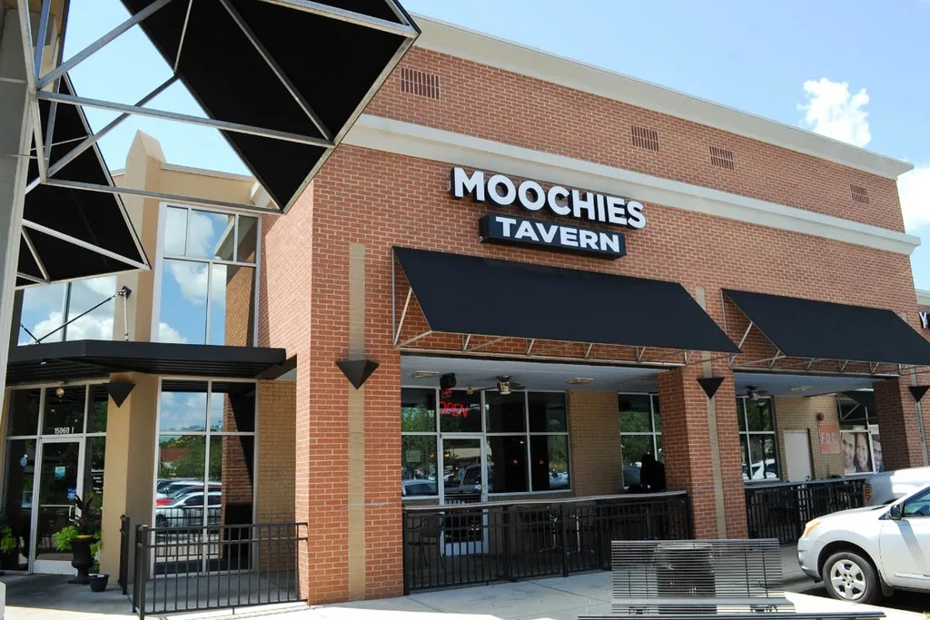 Moochies Tavern's brick exterior, with black awnings, under a sunny sky.