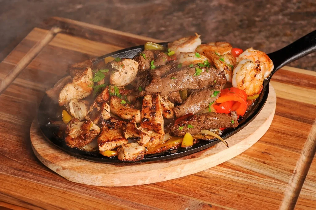 Sizzling chicken, beef, shrimp fajitas with peppers and onions.