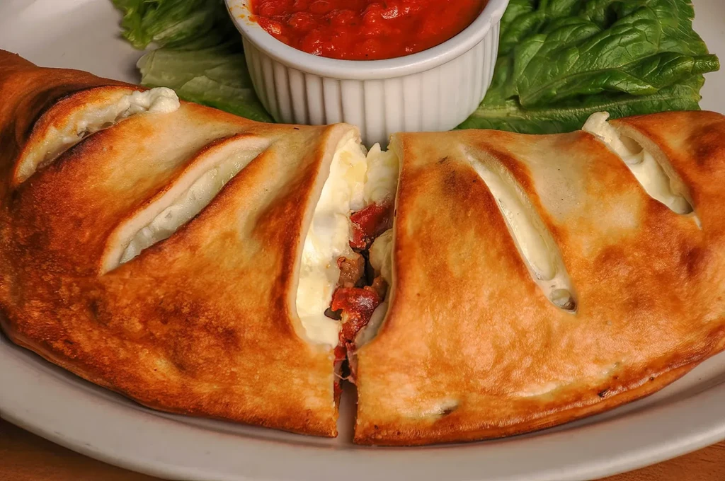 Close-up of a cut calzone revealing cheesy meat filling and marinara.