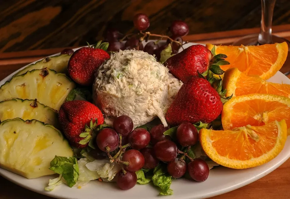 Creamy salad scoop on lettuce, surrounded by colorful fresh fruit.