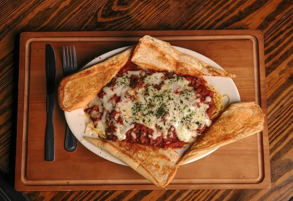 Overhead shot: Spaghetti with meat sauce, melted cheese, bread, and cutlery.
