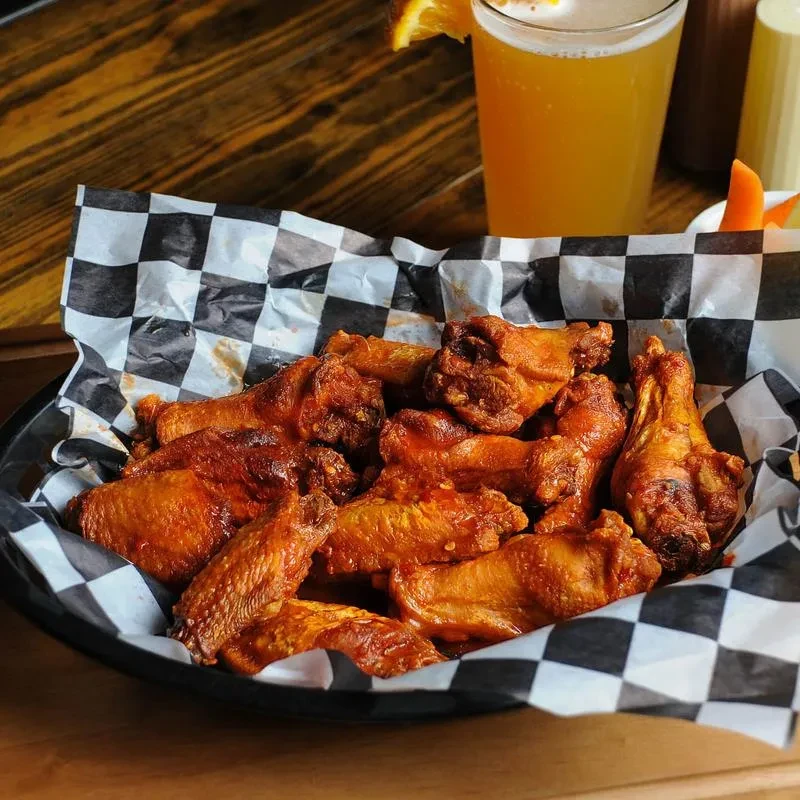 Basket of crispy, sauced chicken wings with beer and sides.