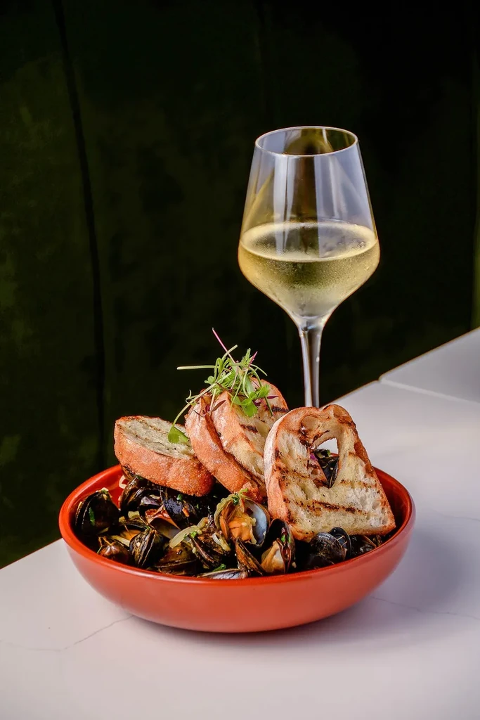 Steamed mussels and clams in a bowl with baguette and white wine.