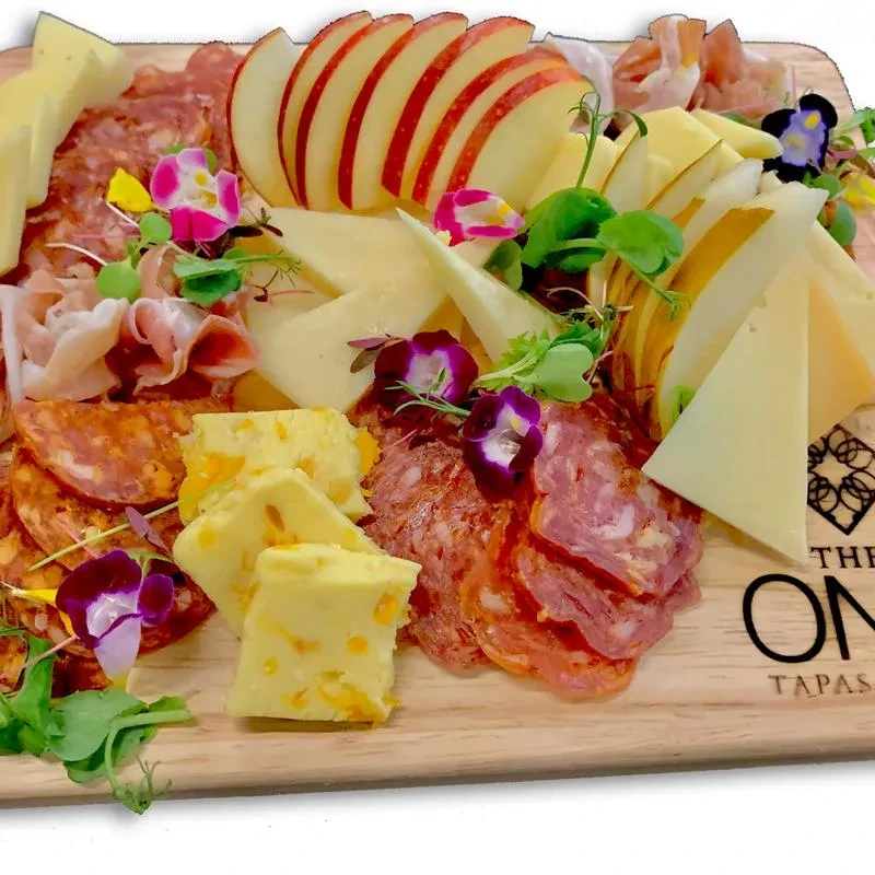Vibrant charcuterie board with meats, cheeses, apples, edible flowers, and microgreens.