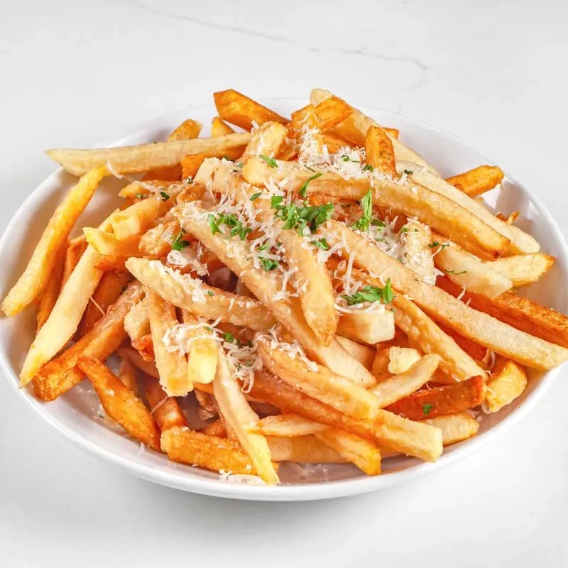 Bowl of golden french fries with Parmesan and green herbs.