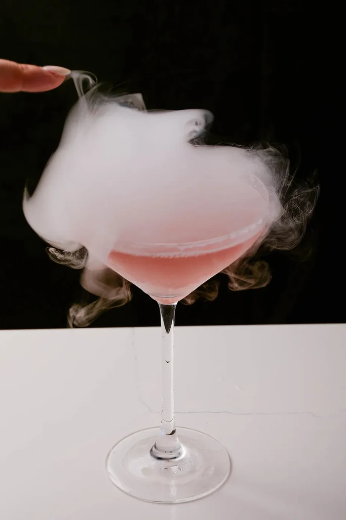 Pink cocktail with dramatic dry ice smoke, a finger visible.