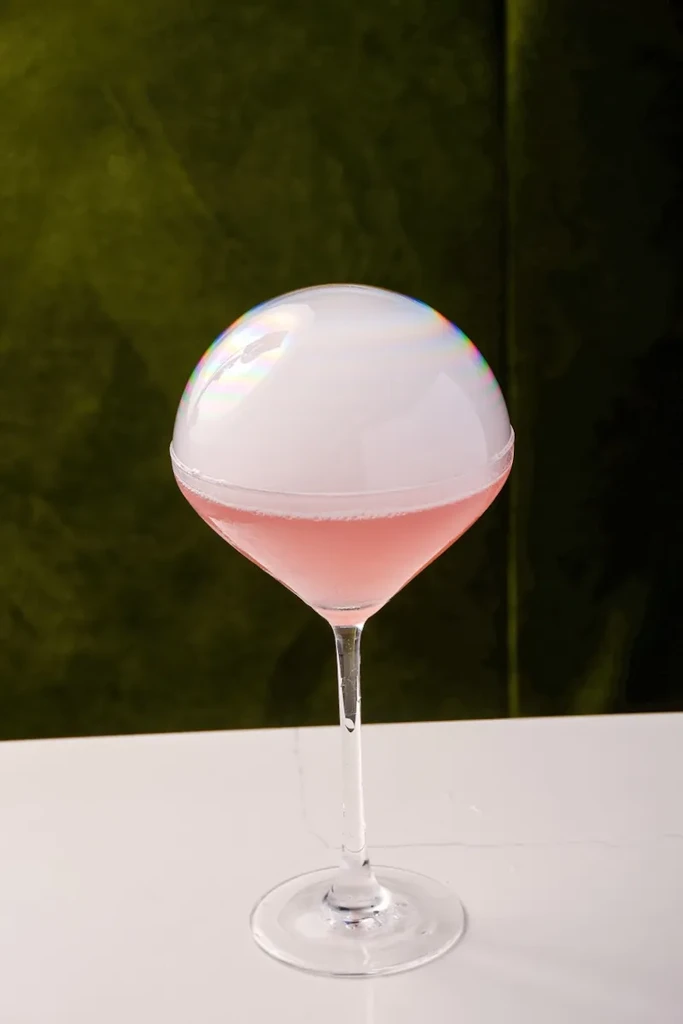 Pink cocktail in martini glass, topped with an iridescent smoke bubble.