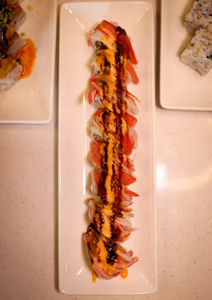 Neatly arranged sushi roll topped with imitation crab and two sauces.