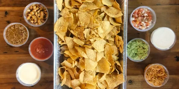 Overhead view of tortilla chips with assorted dips on a wooden table.