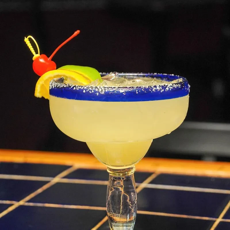Margarita in a classic glass with blue-salted rim and fruit garnishes.