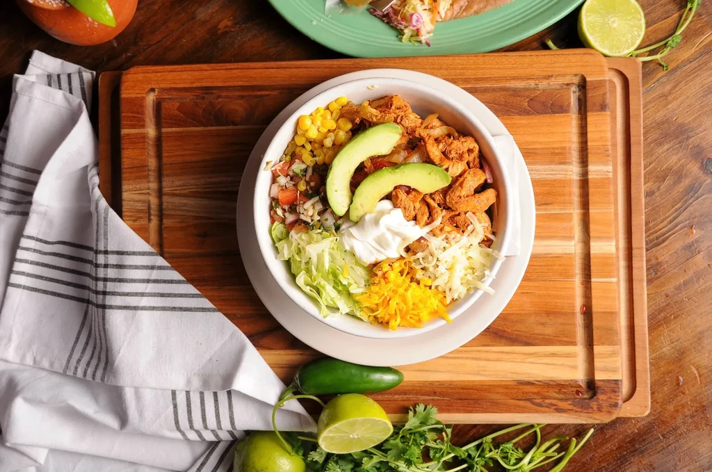 Burrito bowl with chicken, corn, cheese, avocado, lime, and cilantro.