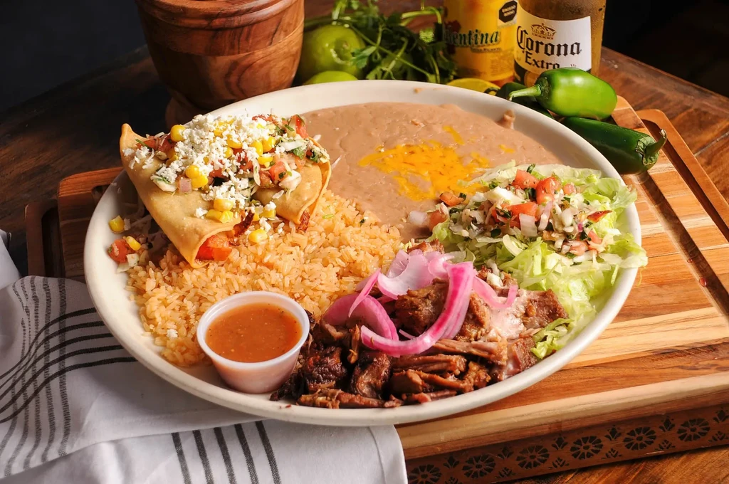 Mexican food plate with flautas, rice, beans, shredded meat, and fresh garnishes.